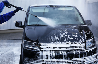 Photo of Worker cleaning automobile with high pressure water jet at car wash, closeup