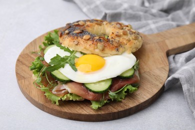 Tasty bagel with cured ham, egg, cucumber and salad mix on light table, closeup