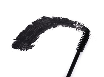 Applicator and black mascara smear on white background, top view