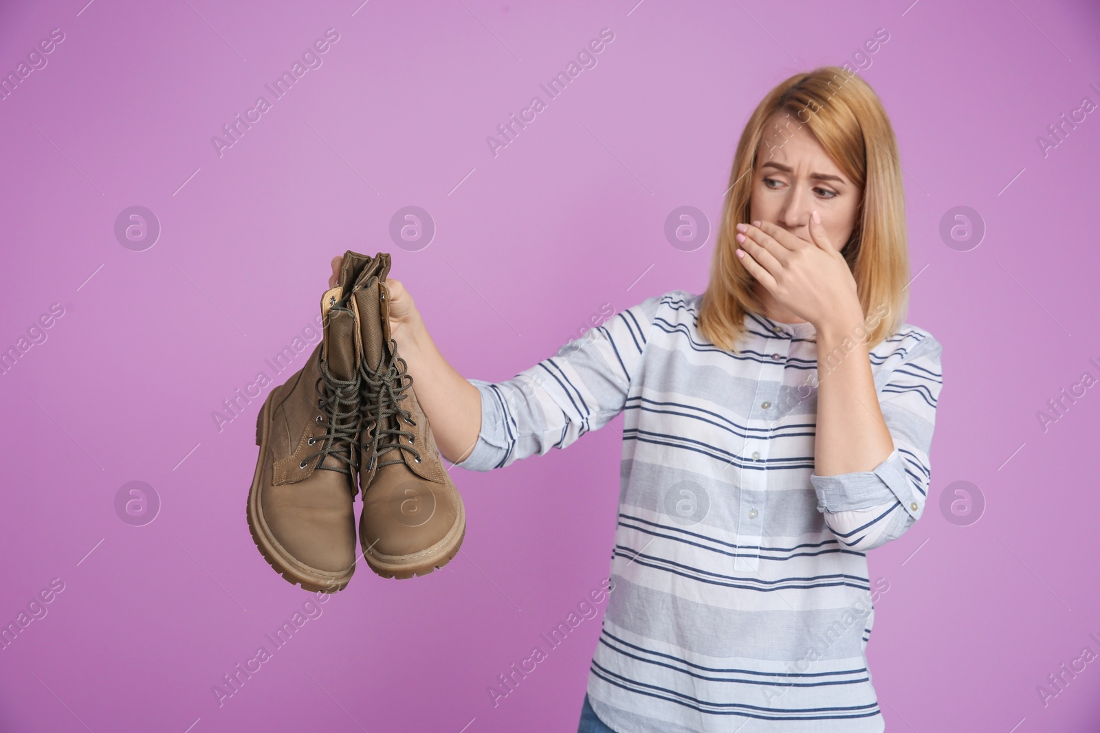 Photo of Young woman with stinky shoes on color background. Air freshener