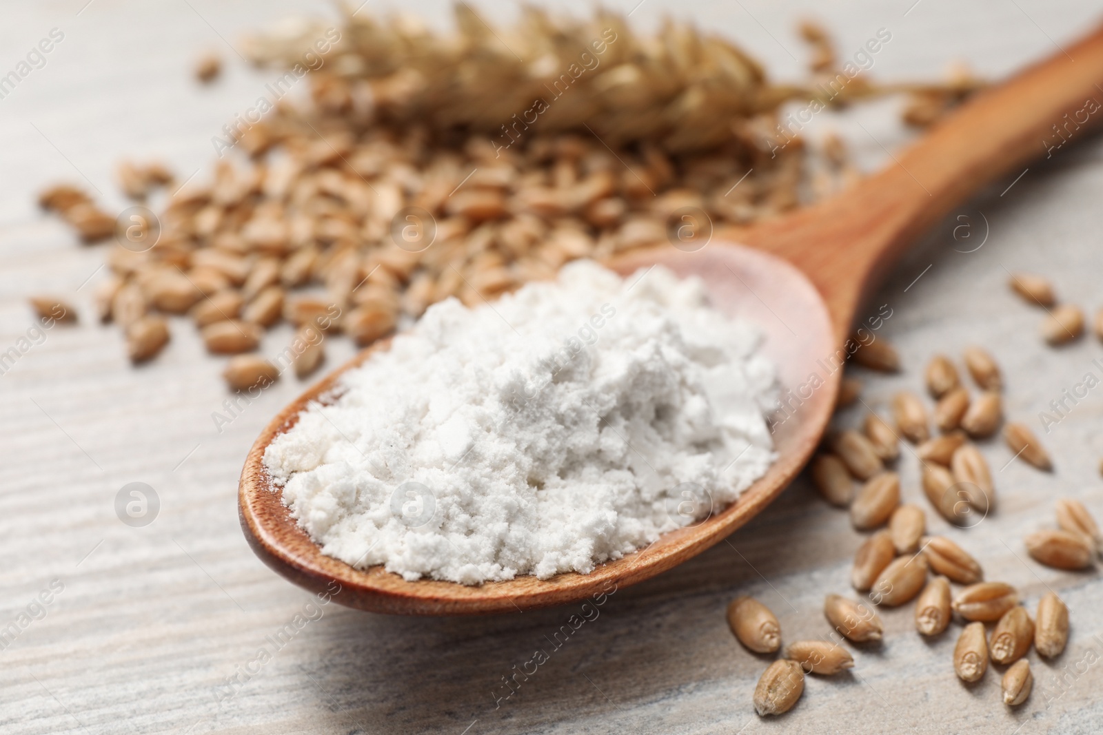 Photo of Spoon with organic flour and grains of wheat on wooden table, closeup