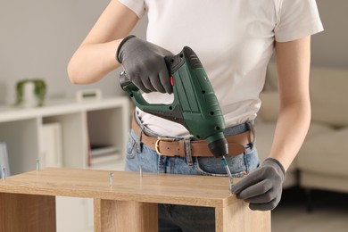 Photo of Young woman with electric screwdriver assembling furniture at home, closeup