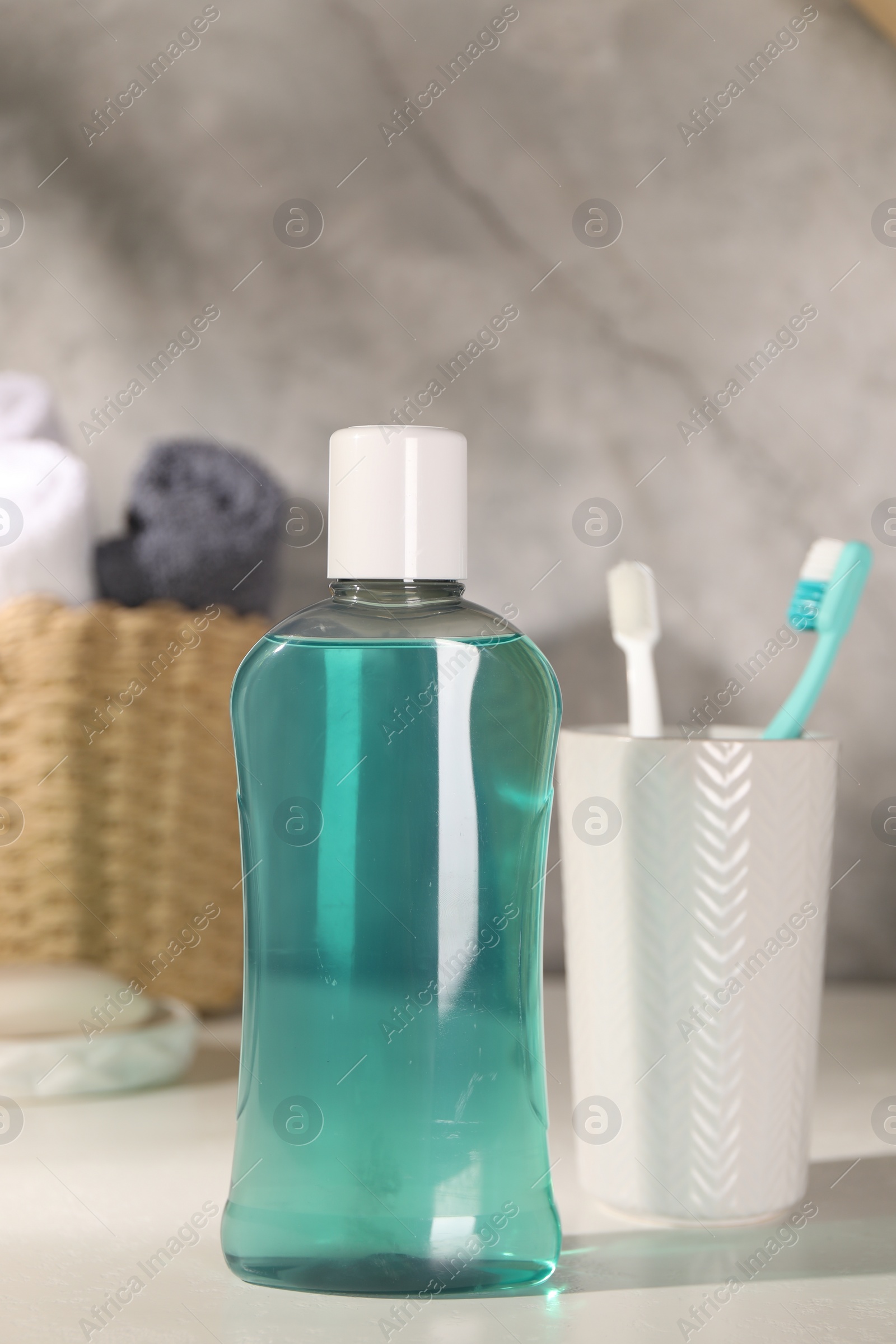 Photo of Bottle of mouthwash and toothbrushes on light table in bathroom
