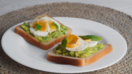 Photo of Tasty sandwiches with boiled egg, avocado and spinach on wicker mat, closeup