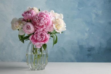 Photo of Beautiful peonies in glass vase on white table. Space for text