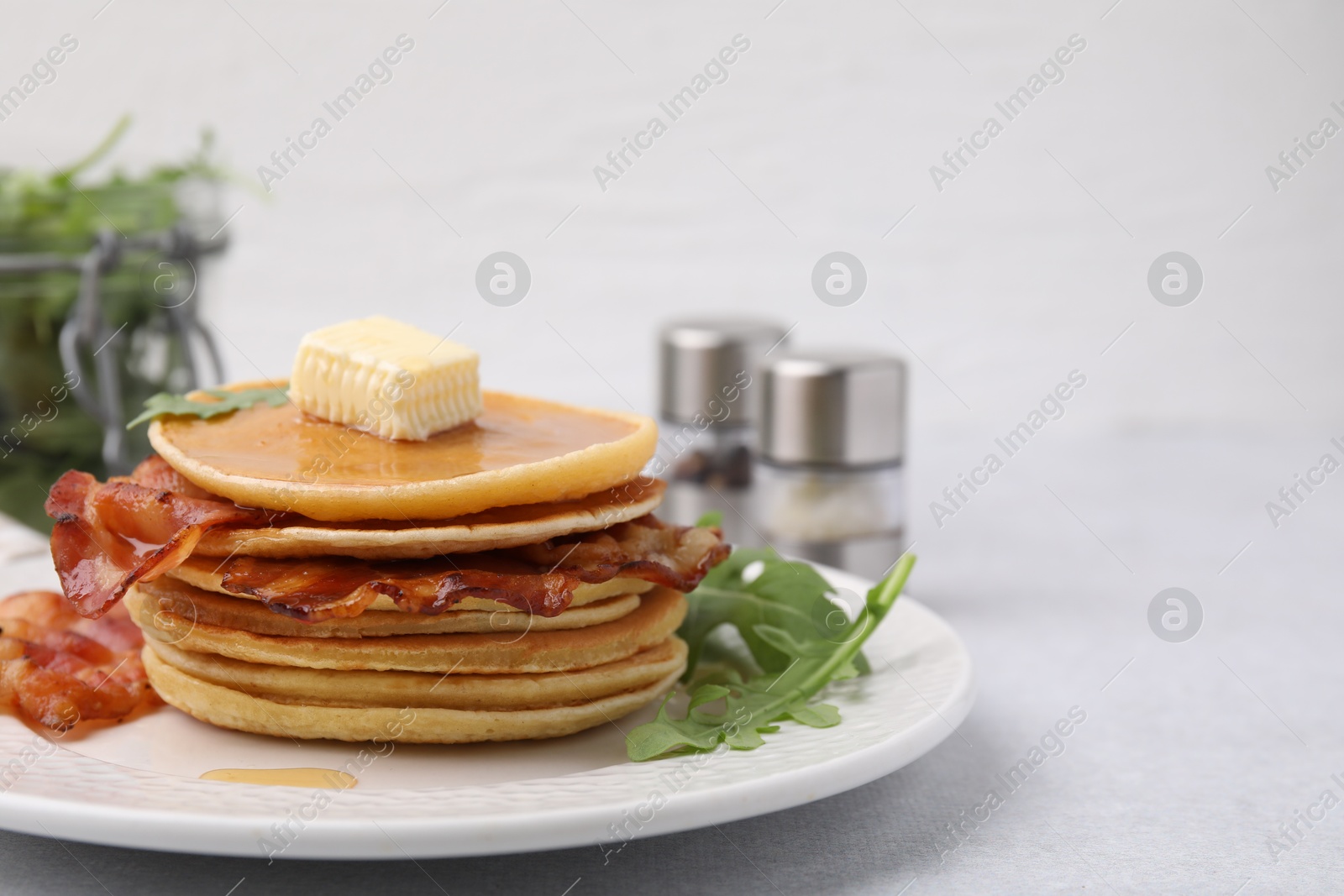 Photo of Delicious pancakes with bacon, butter and arugula on light table, closeup. Space for text