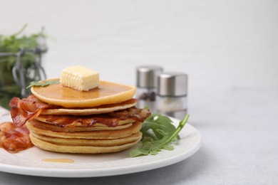 Photo of Delicious pancakes with bacon, butter and arugula on light table, closeup. Space for text