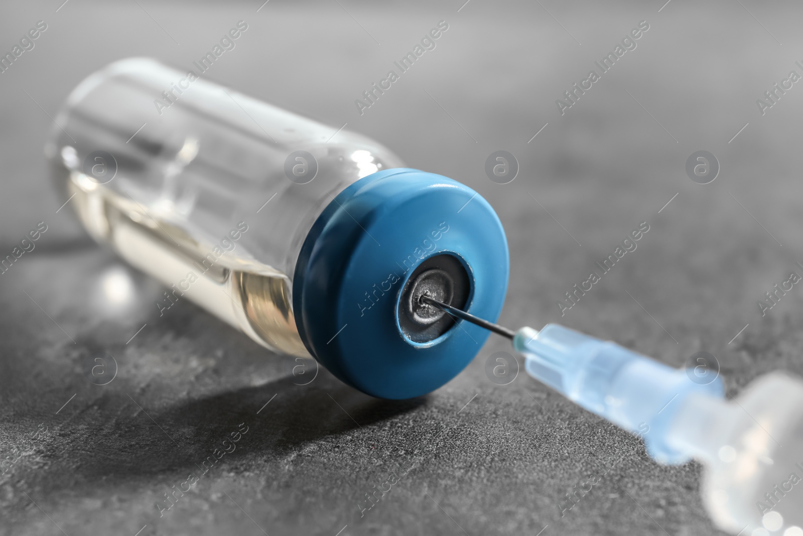 Photo of Vial with vaccine and syringe on grey background, closeup