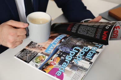 Businessman with cup of coffee reading sports magazine at table, closeup