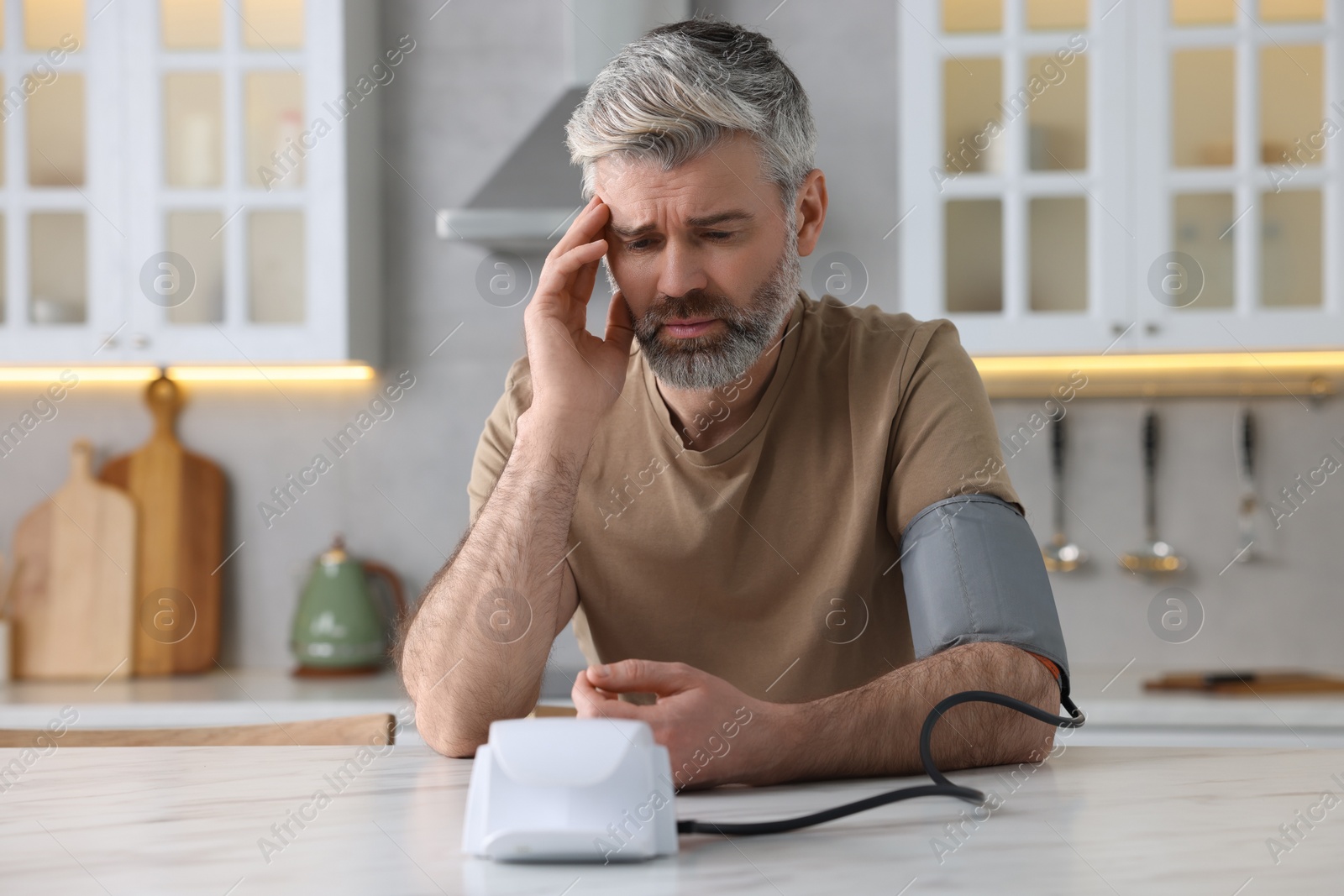 Photo of Man measuring blood pressure at table indoors