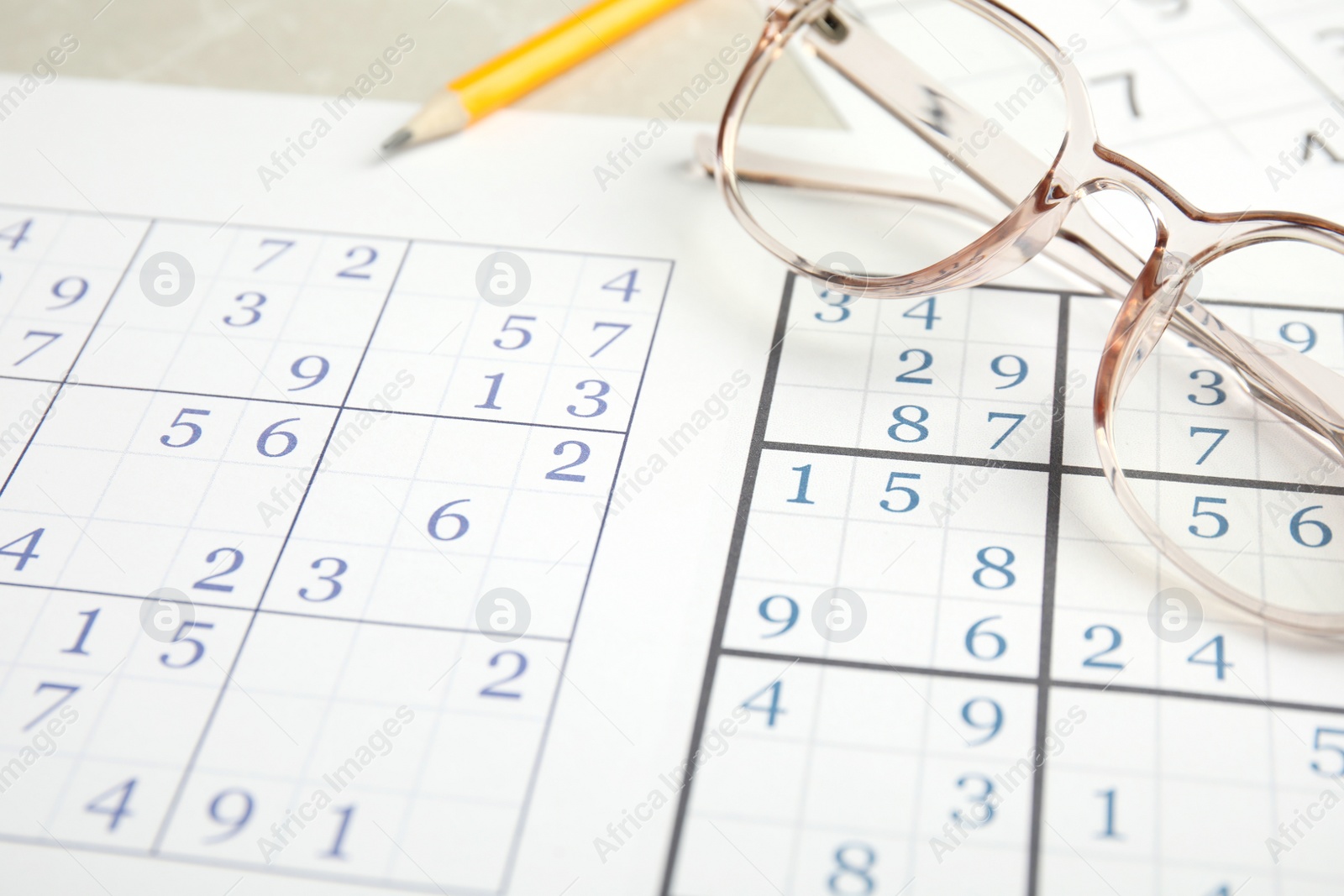 Photo of Sudoku and eyeglasses on table, closeup view