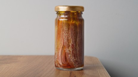 Photo of Jar with anchovy fillets in oil on wooden table