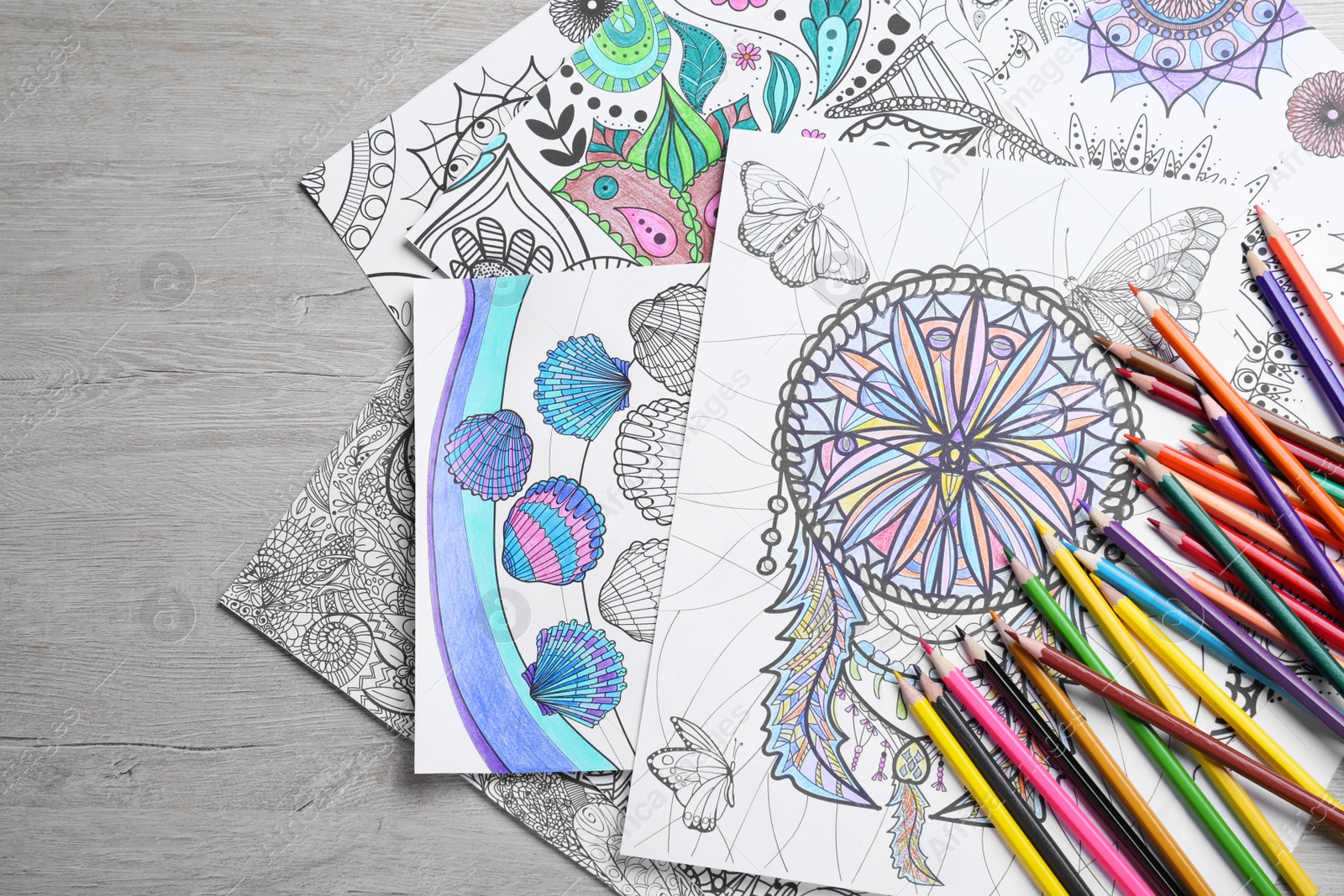 Photo of Antistress coloring pages and pencils on light wooden table, flat lay