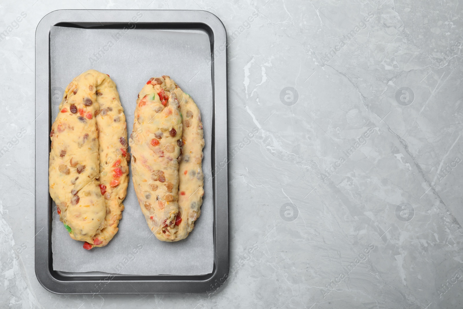 Photo of Top view of baking tray with raw homemade Stollens on grey marble table, space for text. Traditional German Christmas bread