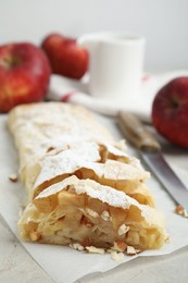 Photo of Delicious apple strudel with almonds and powdered sugar on light grey table, closeup. Space for text