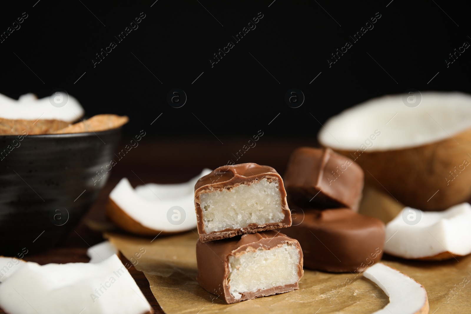 Photo of Delicious milk chocolate candy bars with coconut filling on wooden table, closeup. Space for text