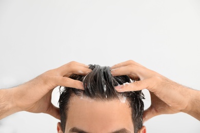 Photo of Man applying shampoo onto his hair against light background, closeup. Space for text
