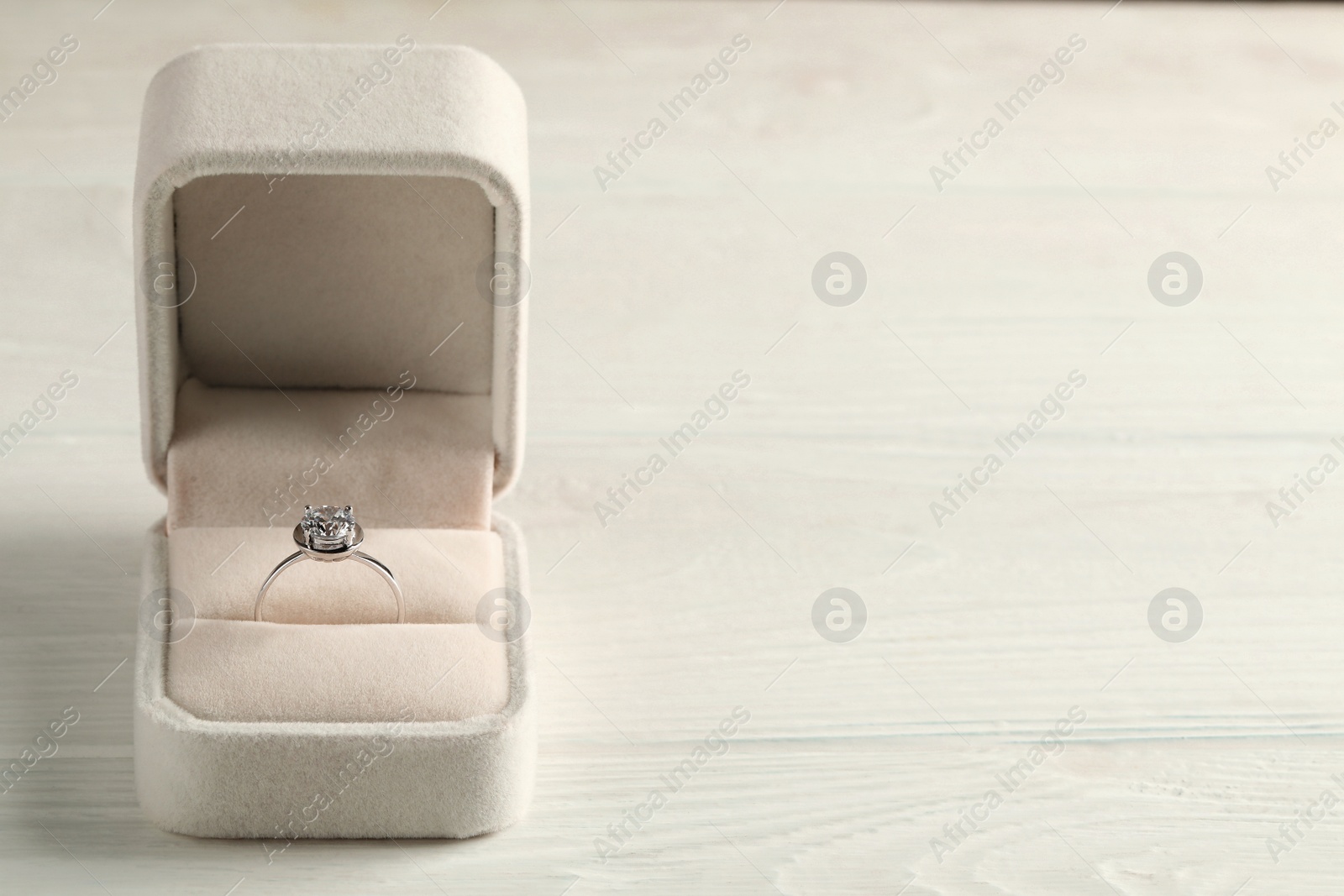 Photo of Beautiful engagement ring in box on white wooden table, space for text