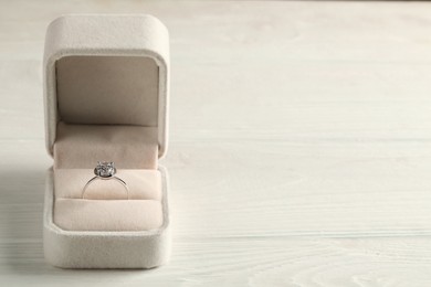 Beautiful engagement ring in box on white wooden table, space for text