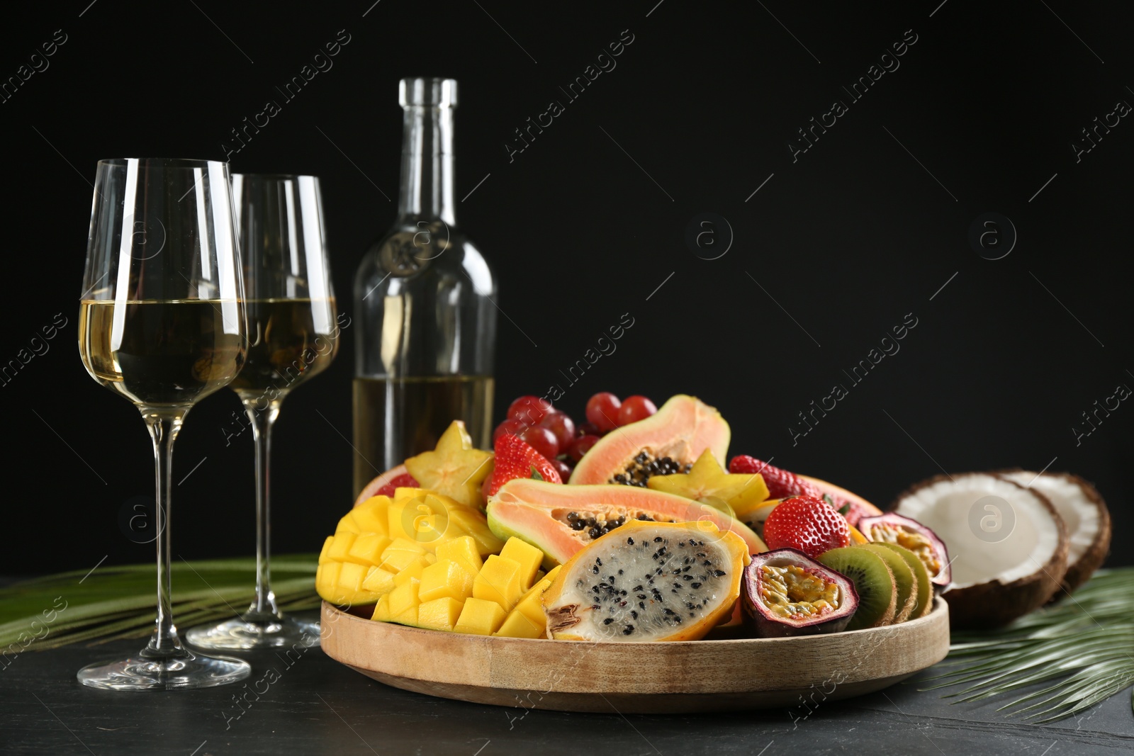 Photo of Delicious exotic fruits and glasses of wine on black table