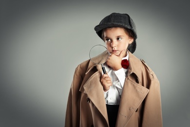 Cute little child in hat with magnifying glass playing detective on grey background, space for text