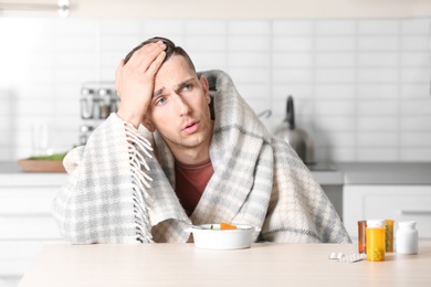 Photo of Sick young man eating broth to cure cold at table in kitchen