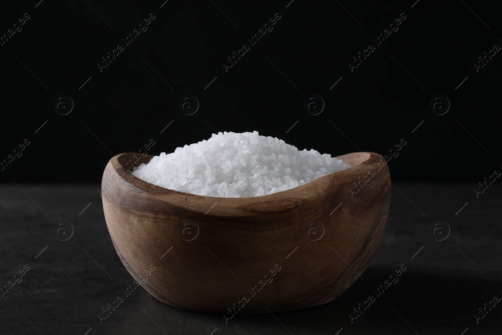 Photo of Natural salt in wooden bowl on dark grey table