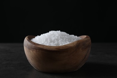 Natural salt in wooden bowl on dark grey table