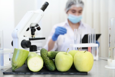 Fresh vegetables, fruits on table and scientist proceeding quality control in laboratory