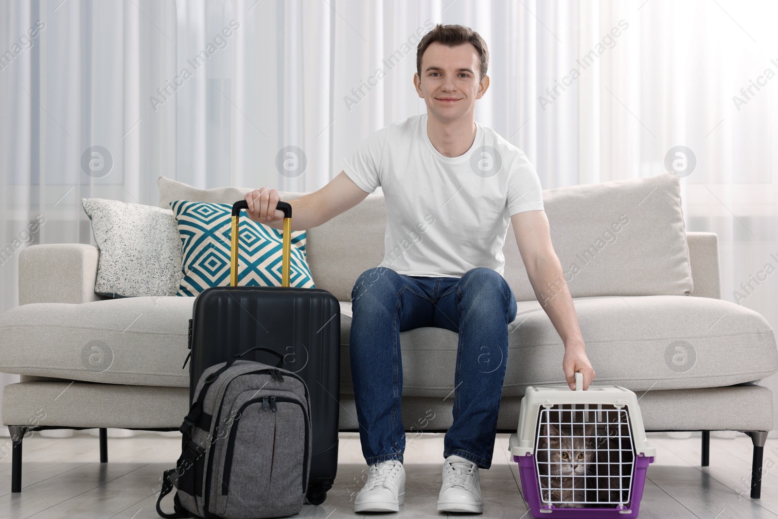 Photo of Travel with pet. Man near carrier with cute cat on sofa at home