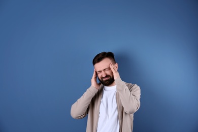 Portrait of handsome bearded man suffering from headache on color background