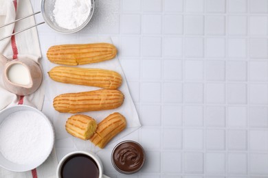Photo of Delicious eclairs, chocolate paste and coffee on white checkered table, flat lay. Space for text