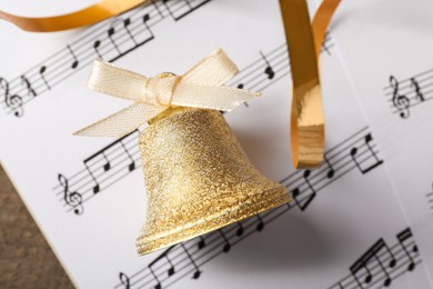 Photo of Golden bell and music sheets on wooden table, closeup. Christmas decor