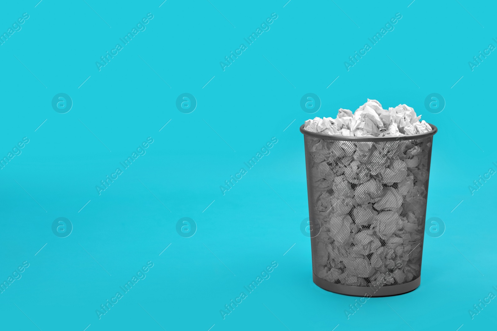 Photo of Metal bin with crumpled paper on color background, space for text