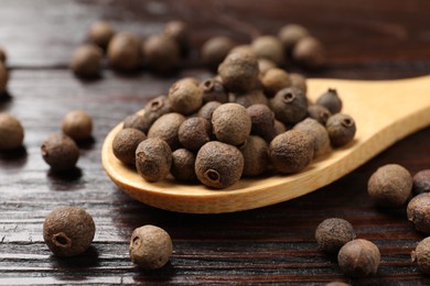 Photo of Dry allspice berries (Jamaica pepper) and spoon on wooden table, closeup