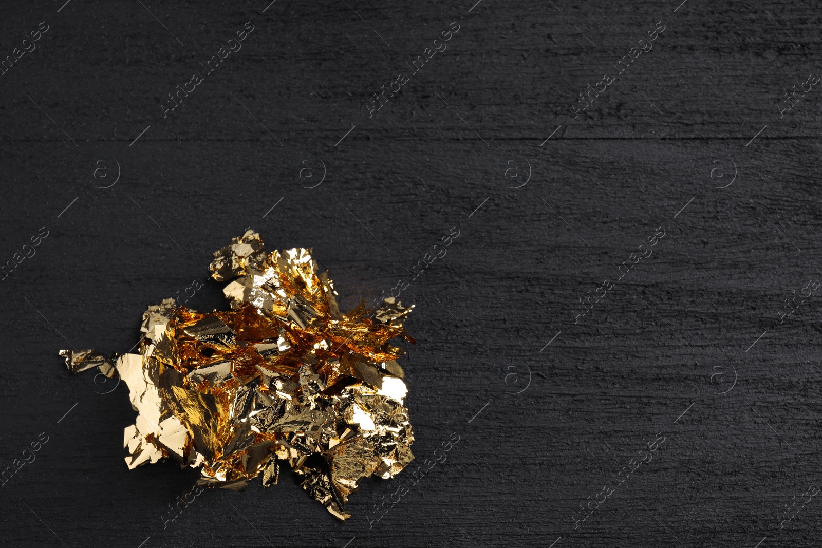 Photo of Pieces of edible gold leaf on black wooden table, top view. Space for text