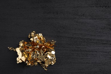 Pieces of edible gold leaf on black wooden table, top view. Space for text