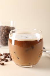 Photo of Refreshing iced coffee with milk in glass and beans on beige background, space for text