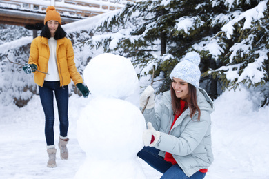 Happy friends making snowman outdoors. Winter vacation