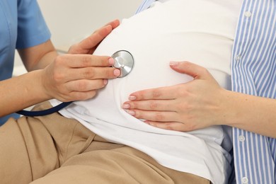 Photo of Pregnancy checkup. Doctor with stethoscope listening baby's heartbeat in patient's tummy in clinic, closeup