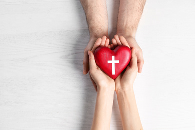 Image of Couple holding heart with cross symbol on wooden background, top view. Christian religion