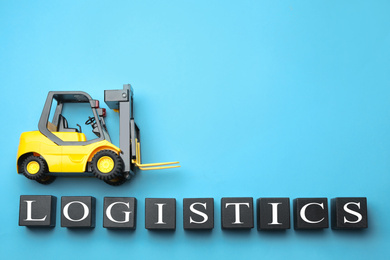 Photo of Flat lay composition with toy forklift and word LOGISTICS on light blue background, space for text. Wholesale concept