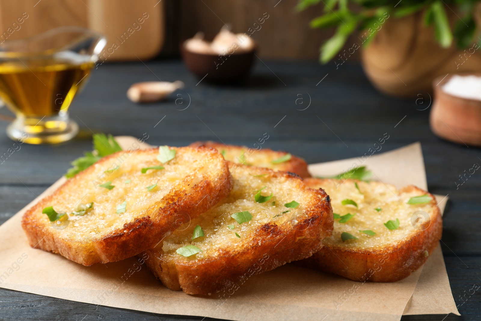 Photo of Slices of delicious toasted bread with garlic and herbs on blue wooden table, closeup