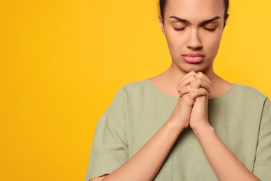 African American woman with clasped hands praying to God on orange background. Space for text