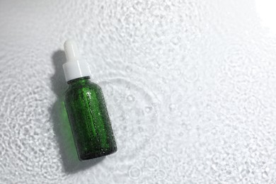 Bottle of cosmetic product in water on white background, top view. Space for text