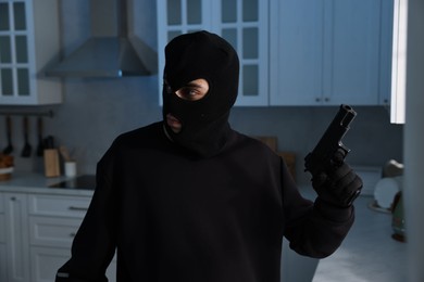 Photo of Thief wearing balaclava with gun in foreign house. Burglary