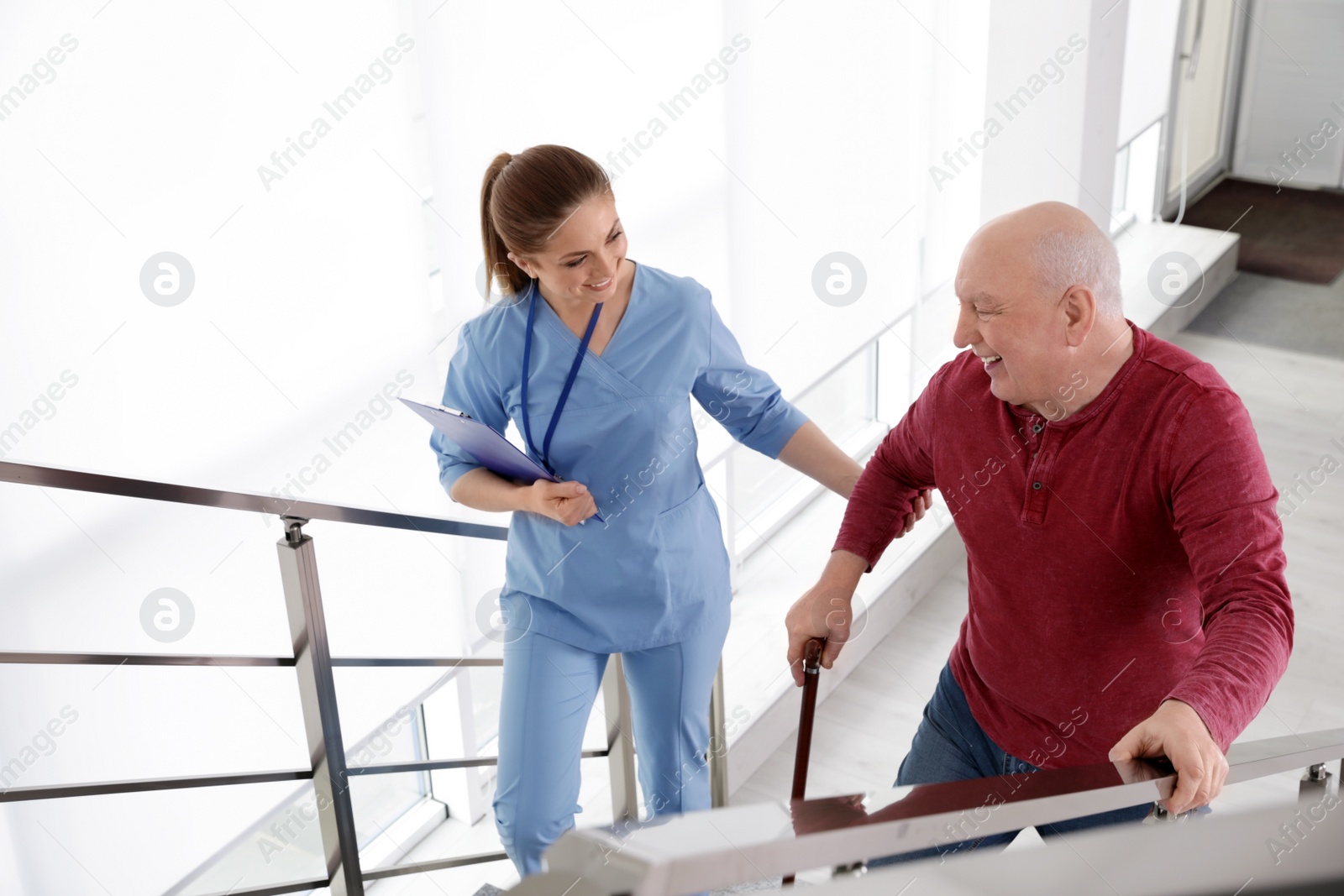 Photo of Nurse assisting senior man with cane to go up stairs indoors