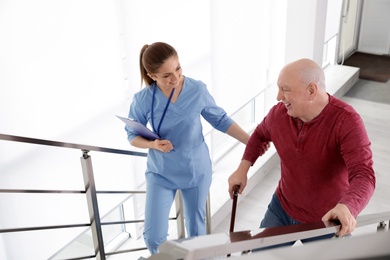 Nurse assisting senior man with cane to go up stairs indoors