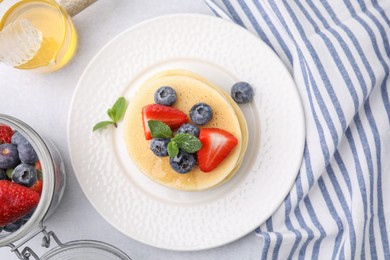 Delicious pancakes with strawberries, blueberries and honey on light grey table, flat lay