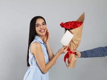 Photo of Happy woman receiving red tulip bouquet and greeting card from man on light grey background. 8th of March celebration